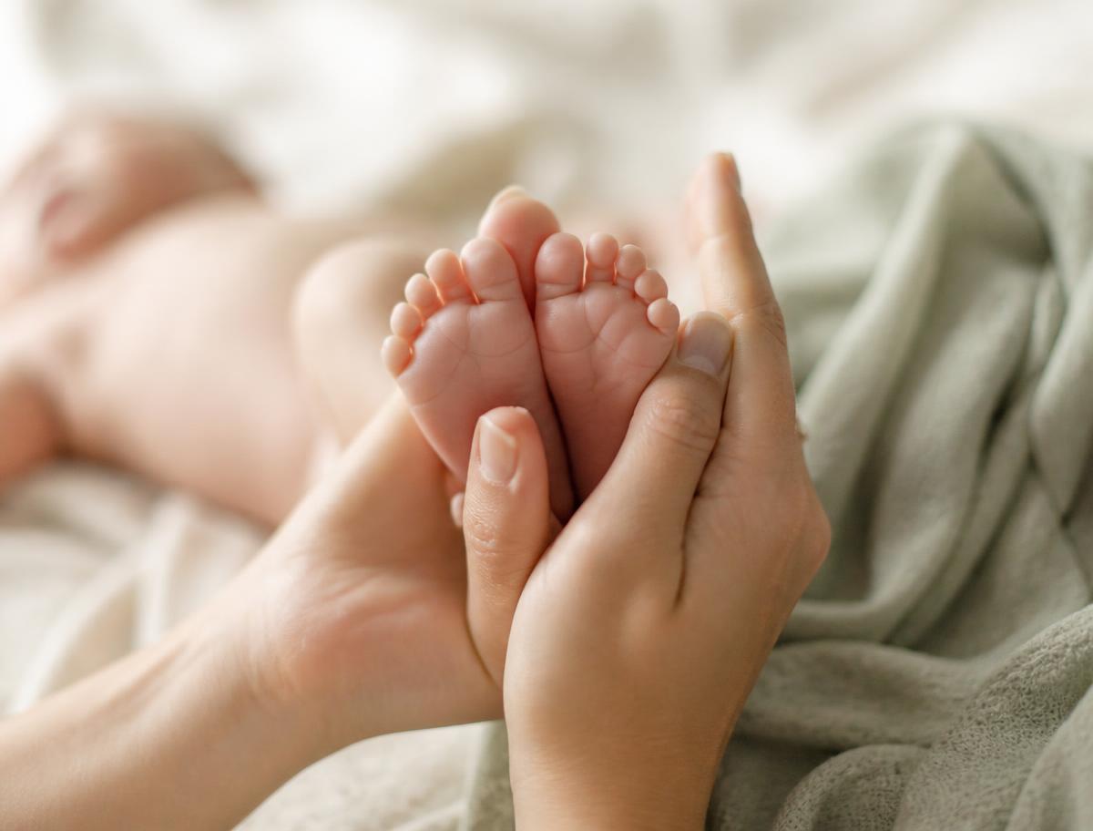 Mãos de um adulto segurando com carinho os pés de um recém-nascido